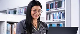 Persona sentada frente a un computador, con estantes llenos de libros al fondo.